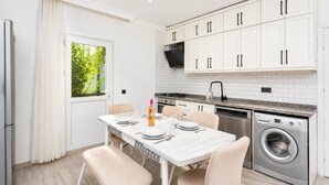 A modern kitchen with white cabinets, a built-in washing machine, and a dining area with a table set for four. - Daisy Villa - Five Bedroom Villa, Sleeps 10 (Dalyan)