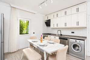 Cocina moderna con armarios blancos, lavadora integrada y comedor con mesa lista para cuatro.