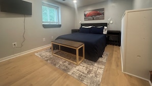 A bedroom with a bed, bedside tables, a desk, a window with blinds, a wall-mounted TV, and a painting. - Cozy & Quiet Home Away From Home - 3 Bed, 2 Bath, 4 Beds!! (Indianapolis)