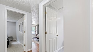 A hallway with white doors, a carpeted floor, and a view into a living room with a sofa and coffee table. - Cozy & Quiet Home Away From Home - 3 Bed, 2 Bath, 4 Beds!! (Indianapolis)