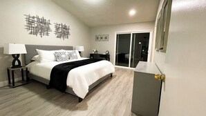 A modern bedroom with a bed, two bedside tables, a desk, and a sliding glass door leading to a balcony. - Relaxed Cozy Pool House (Bakersfield)