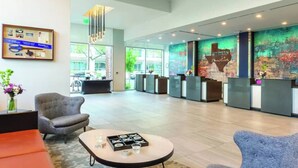 A modern hotel lobby with a reception desk, seating area, and a large window offering a view of the outdoors.