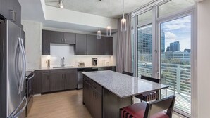 A modern kitchen with a large island, dark cabinetry, and a city view through large windows.