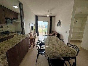 A modern kitchen with a granite countertop, wooden cabinets, and a dining area with a long table and chairs. - FOURTH FLOOR SEA VIEW WITH HEATED OUTDOOR POOL. (Praia Grande Ubatuba)