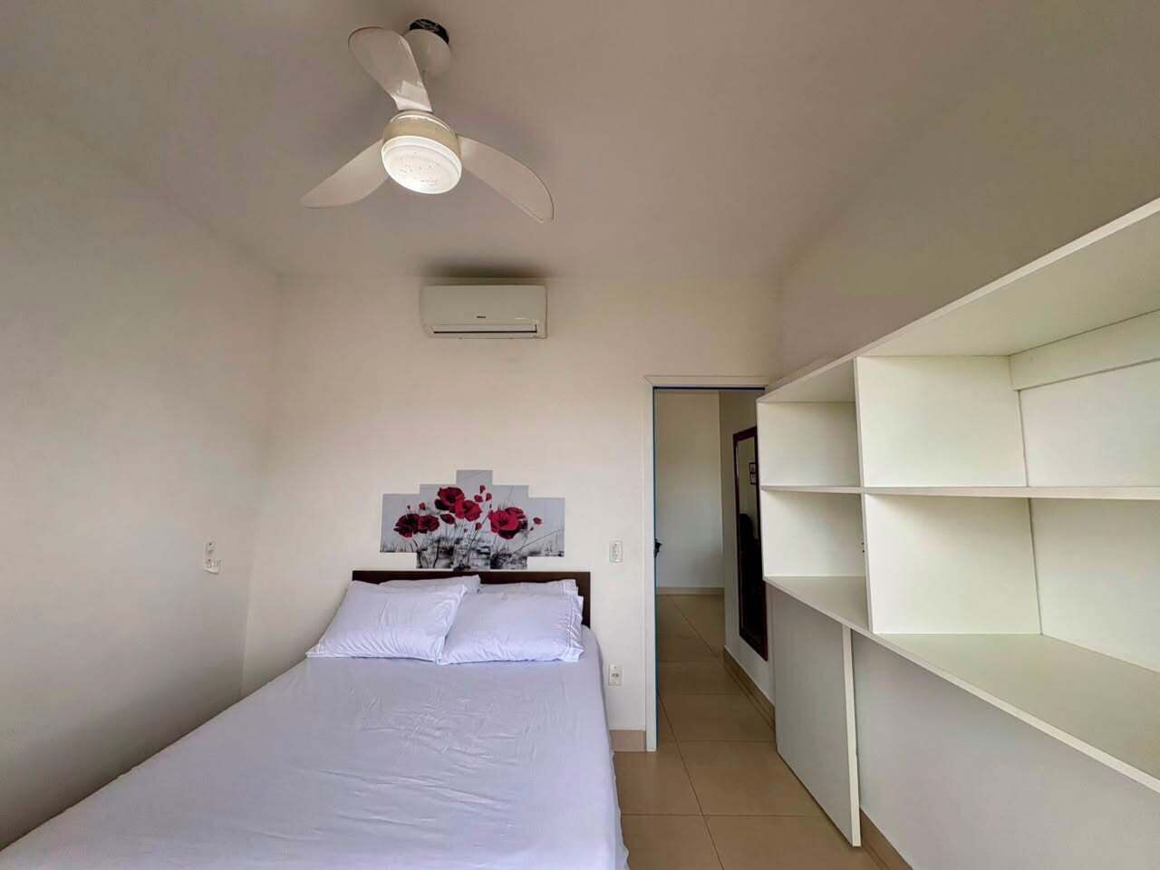 A bedroom with a bed, a ceiling fan, a wall-mounted air conditioner, and a hallway leading to another room.