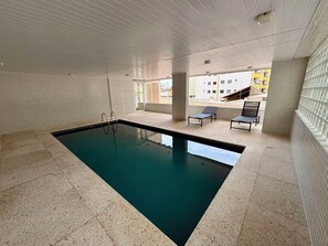 Una piscina interior con paredes y suelo de baldosas, una escalera de piscina y dos sillones de descanso.