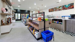 A grocery store interior with shelves stocked with various products, a blue shopping basket, and a counter with a coffee machine.