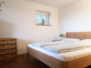 Un dormitorio con una cama de madera, una mesita de noche con lámpara, una ventana con persianas y un aparador de madera.