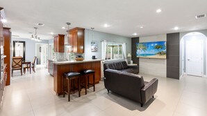 A modern kitchen with a central island, bar stools, and a dining area with chairs. - Central Home in Marco Paradise - Quick to public BEACH (Marco Island)