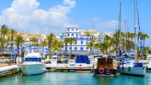 A marina with boats docked, a building with blue and white architecture, and palm trees. - Apartment 'Modern Marina Apt Fantastic' with Sea View, Wi-Fi and Air Conditioning (Estepona)