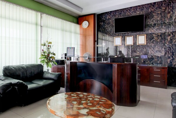 A reception area with a wooden desk, a clock, framed certificates, and a large TV on the wall.