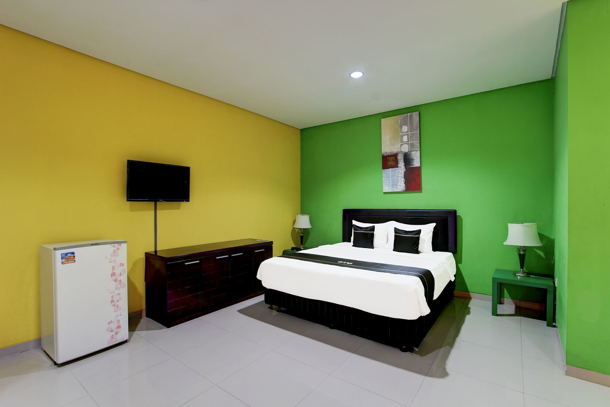 Un dormitorio con cama, televisor, refrigerador y pared verde.