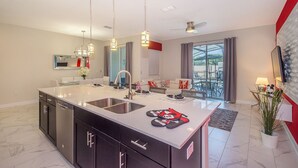 Une cuisine moderne dotée d’un grand îlot central, d’appareils électroménagers en acier inoxydable et de luminaires suspendus.