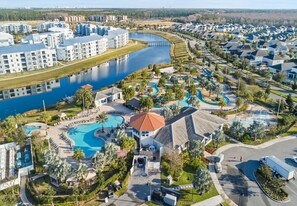 Eine Luftaufnahme eines Resorts mit mehreren Schwimmbecken, einem zentralen Gebäude mit rotem Dach und einem Gewässer.