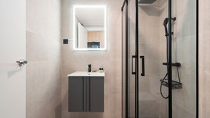 Un baño moderno con cabina de ducha de vidrio, tocador con espejo y un lavamanos pequeño.
