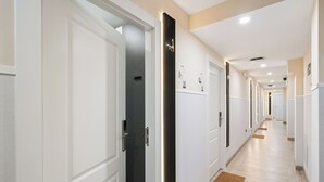 Un pasillo de hotel con puertas blancas, un elemento de iluminación vertical y suelo de madera.