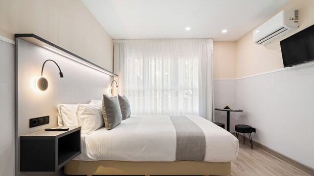 Una habitación de hotel moderna con una cama grande, mesitas de noche, una pequeña mesa y un televisor.