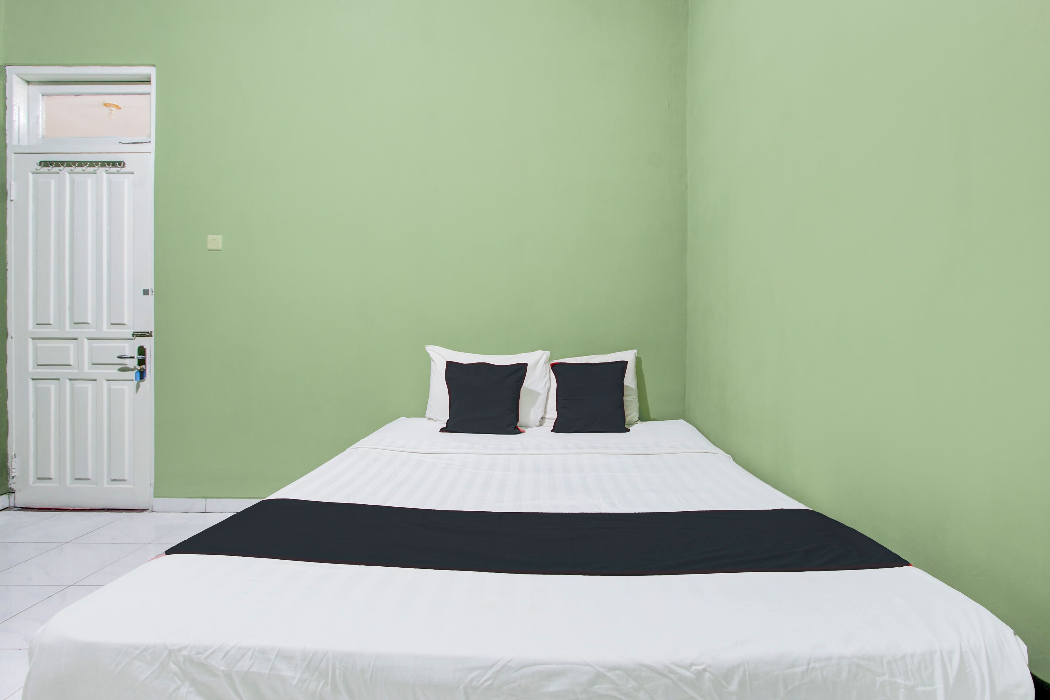 A single bed with a white and black bedspread, two black pillows, and a white headboard in a room with green walls and a white door.