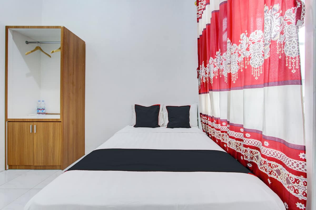 Un dormitorio con cama, dos almohadas negras, un armario de madera y una cortina roja estampada.