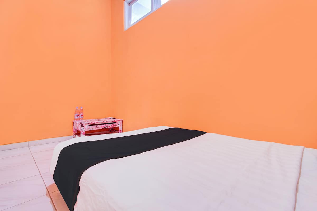 Una habitación con una cama, una mesita con botellas y una ventana.