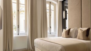Une chambre à coucher avec un grand lit, deux fenêtres avec des rideaux, un radiateur et un luminaire fixé au mur.