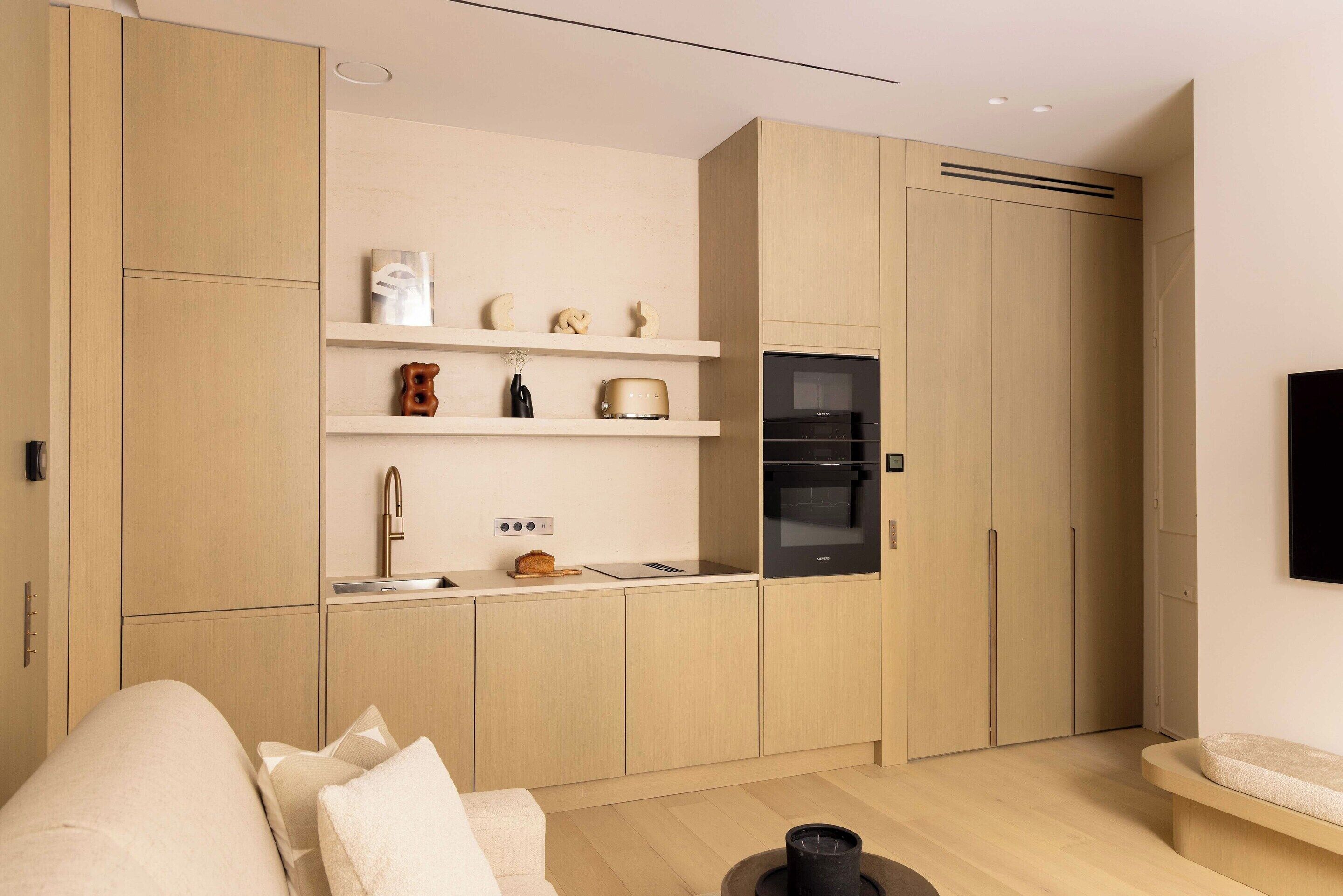 A modern kitchen with wooden cabinets, a built-in oven, and a microwave. There is a countertop with a sink and a toaster.