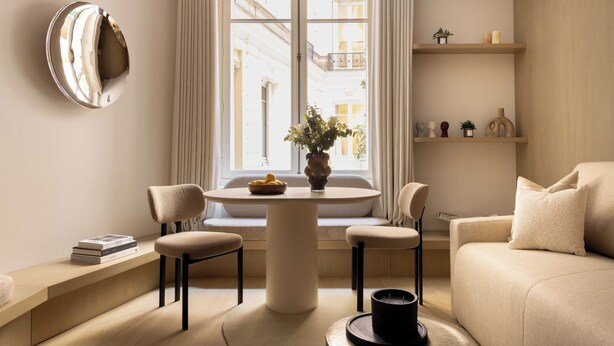 Un salon moderne comprenant une table ronde, deux chaises, un canapé, une fenêtre avec des rideaux et une étagère murale agrémentée d’objets décoratifs.