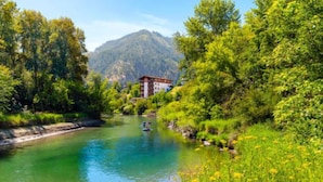 Un río con una casa en la orilla, rodeada de vegetación y montañas al fondo.
