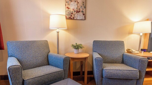 Habitación de hotel con dos sillones, una mesita redonda con una planta y una lámpara a cada lado.
