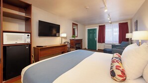 Una habitación de hotel con una cama, un escritorio, un microondas, un televisor, una chimenea y un sofá.