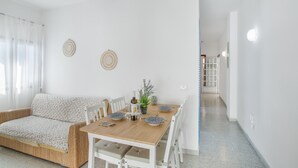 Een moderne woonkamer met een houten eettafel, witte stoelen, een bank en een kleine potplant.
