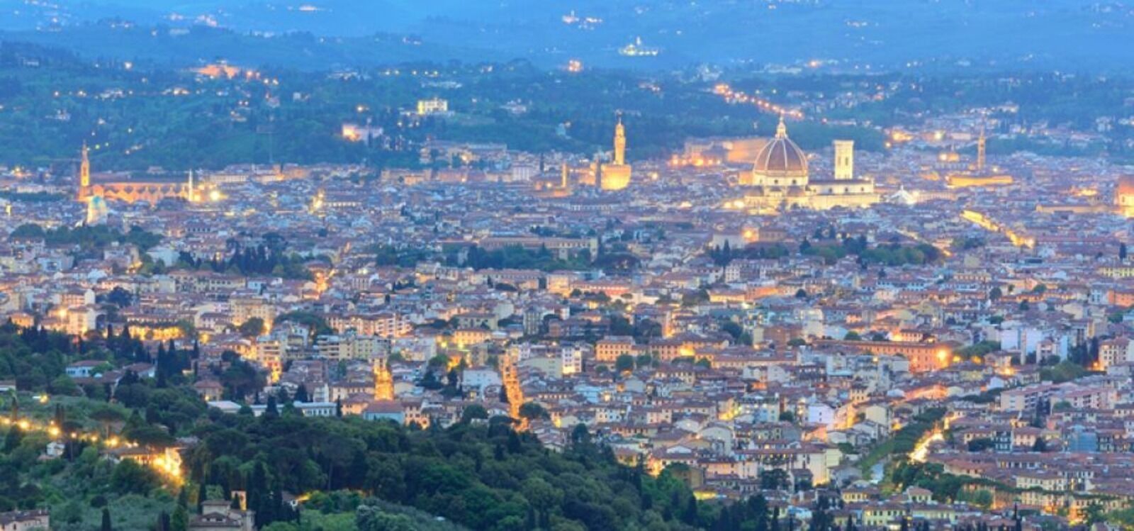 A panoramic view of a cityscape at dusk with illuminated buildings and prominent historical architecture.