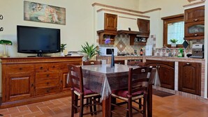 A kitchen with wooden cabinets, a tiled backsplash, a dining table with chairs, a television, and a microwave. - Tuscan Barn 15 min from Florence, Parking, Garden (Pian di Mugnone)