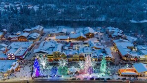Un village enneigé, avec des bâtiments traditionnels en bois et une place centrale illuminée de guirlandes colorées.