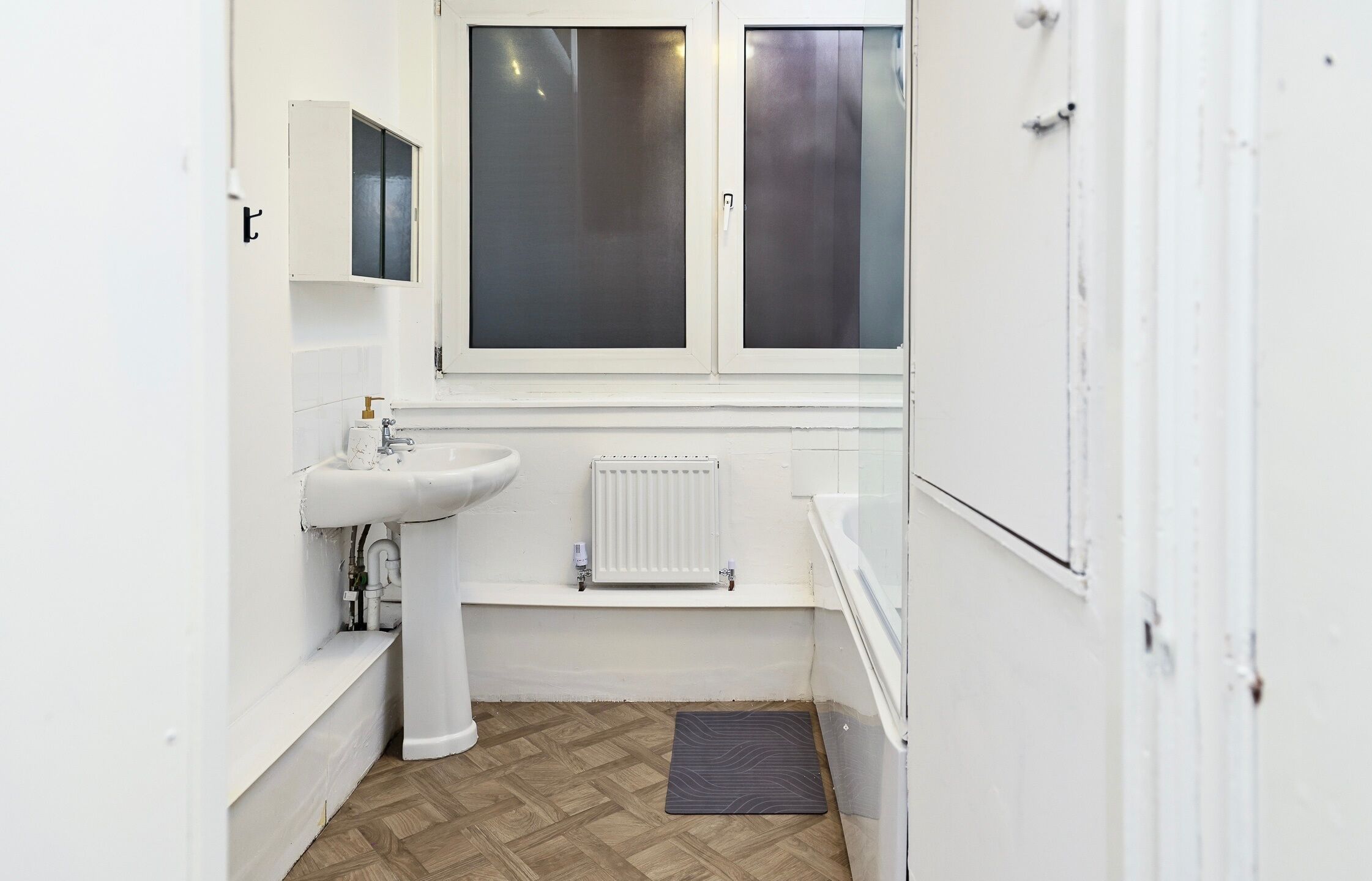A small, white bathroom with a sink, mirror, and window.