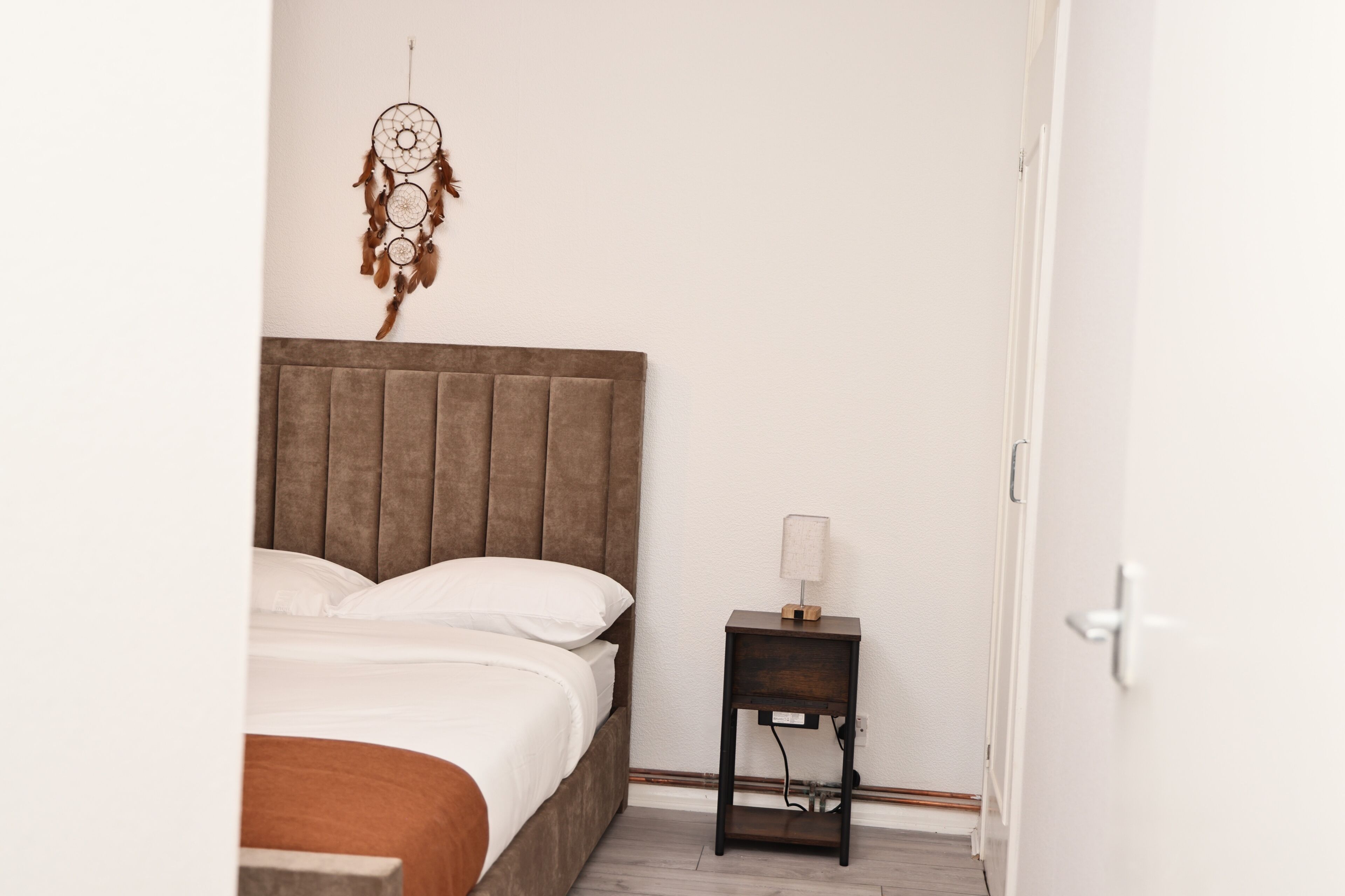 A bedroom with a bed, a bedside table, and a wall-mounted dreamcatcher.
