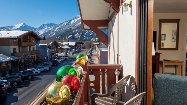 En balkong med utsikt över ett snöklätt berg, en gata med parkerade bilar och färgglada ballonger.