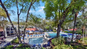 A resort with a swimming pool surrounded by lounge chairs and umbrellas, a covered area with tables and chairs, and lush greenery. - Villa 332: 2  BR, 1.5  BA Condominium in Jekyll Island, Sleeps 6 (Jekyll Island)