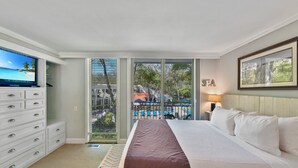 A hotel room with a bed, a TV, a dresser, and a balcony with a view of the sea. - Villa 332: 2  BR, 1.5  BA Condominium in Jekyll Island, Sleeps 6 (Jekyll Island)