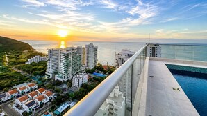 A high-rise building with a pool, overlooking a coastal area with a sunset.