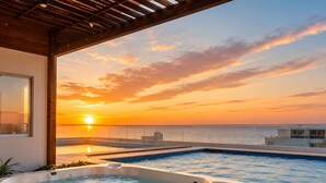 A rooftop pool with a hot tub, a sunset view, and a wooden pergola.