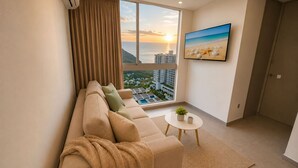 A modern living room with a sofa, a coffee table, a TV, and a large window with a cityscape view. - Apartamentos Salguero Sunset - by SOHO (Santa Marta)