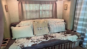 Un intérieur de camping-car chaleureux, avec un canapé à carreaux, des coussins décoratifs et une fenêtre ornée de rideaux légers.