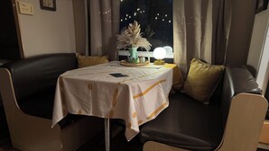 Une pièce chaleureuse avec une table dressée pour deux personnes, un canapé et une fenêtre avec des rideaux.