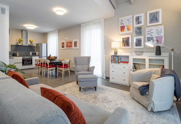 A modern living room with a grey sofa, a checkered armchair, and a dining area with a table and chairs. - Green Lodge - Villa Tortora (Cressa)