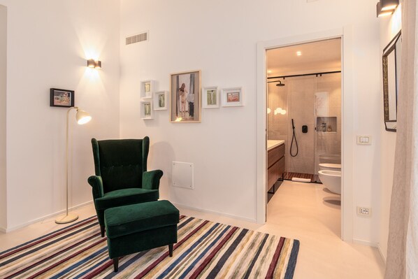 Ein modernes Hotelzimmer mit einem grünen Sessel, einem Streifenmuster-Teppich und einem Badezimmer mit Dusche und Toilette.