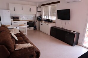 A modern kitchen with white cabinets, a microwave, and a coffee maker. There is a brown sofa with cushions and a flat-screen TV mounted on the wall.