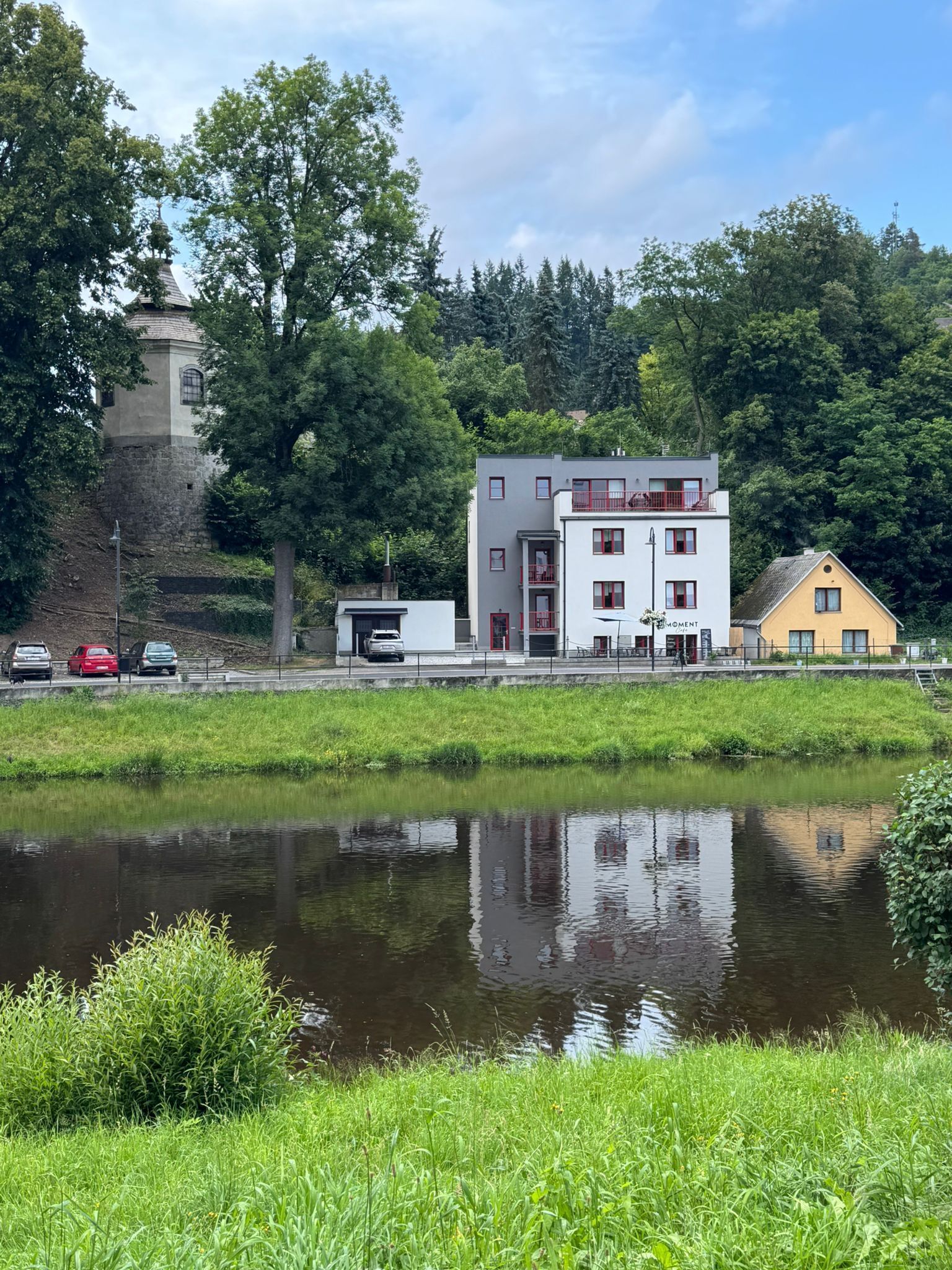 A building with a modern design, featuring a mix of white and grey colors, and a yellow house nearby.