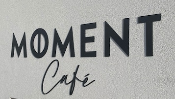 Ein Schild mit den Aufschriften „MOMENT“ und „Cafe“ an einer strukturierten Wand.
