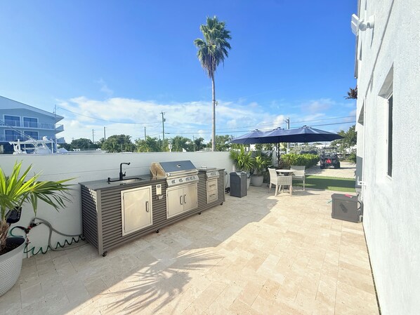 An outdoor patio with a grill, seating, and a view of a building in the background.